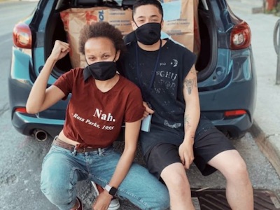 Two of our co-founders sitting in front of a trunk full of grocery bundles.